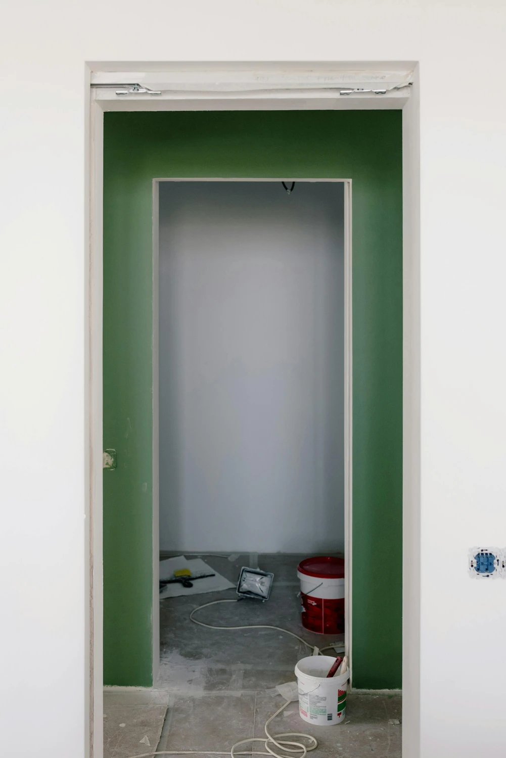 Raumausstatterbetrieb Preukschat - Innenarchitektur und Renovierung - Ein Türrahmen während eines Renovierungsprojekts, mit einer frisch gestrichenen grünen Akzentwand, die einen weißen Türrahmen umgibt.