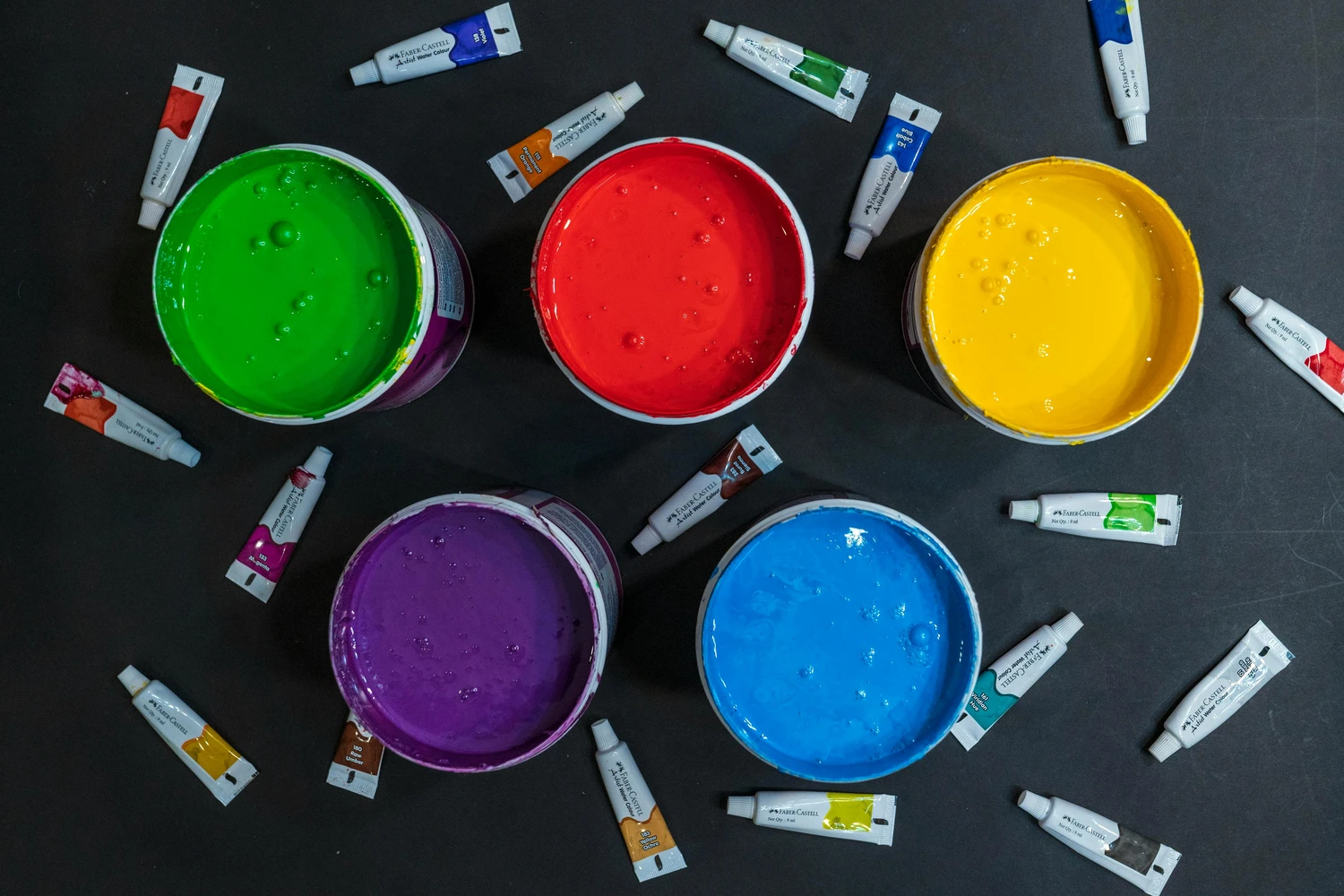 Raumausstatterbetrieb Preukschat - Innenarchitektur und Renovierung - Leuchtende Farben, darunter größere Eimer mit grünen, roten, gelben, violetten und blauen Farben sowie zahlreiche kleinere Tuben mit verschiedenen Farbtönen.